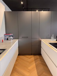 Unsere Ausstellungsküche verbindet modernes Design mit natürlicher Wärme – klare Fronten, edle Materialien und ein schöner Vinylboden in Fischgrätoptik